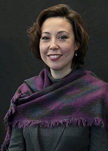 A woman wearing a purple scarf is smiling for the camera.