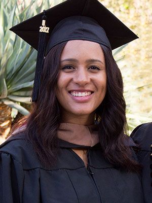 A woman is wearing a graduation cap and gown and smiling.