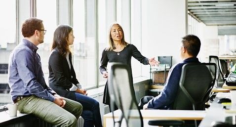 A group of people are sitting around a table in an office having a meeting.