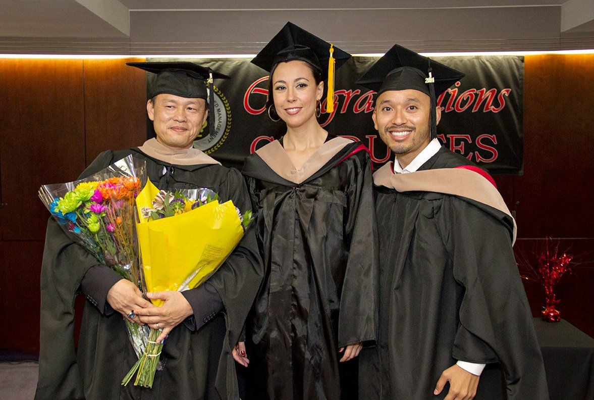 Three graduates are posing for a picture and one of them is holding a bouquet of flowers.