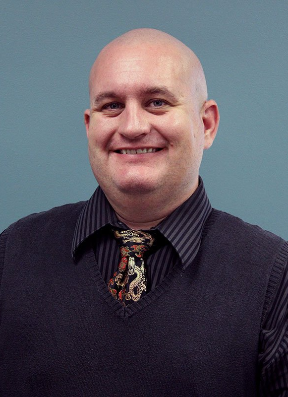 A bald man wearing a striped shirt and tie is smiling for the camera.