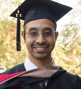 A man wearing a graduation cap and gown is smiling