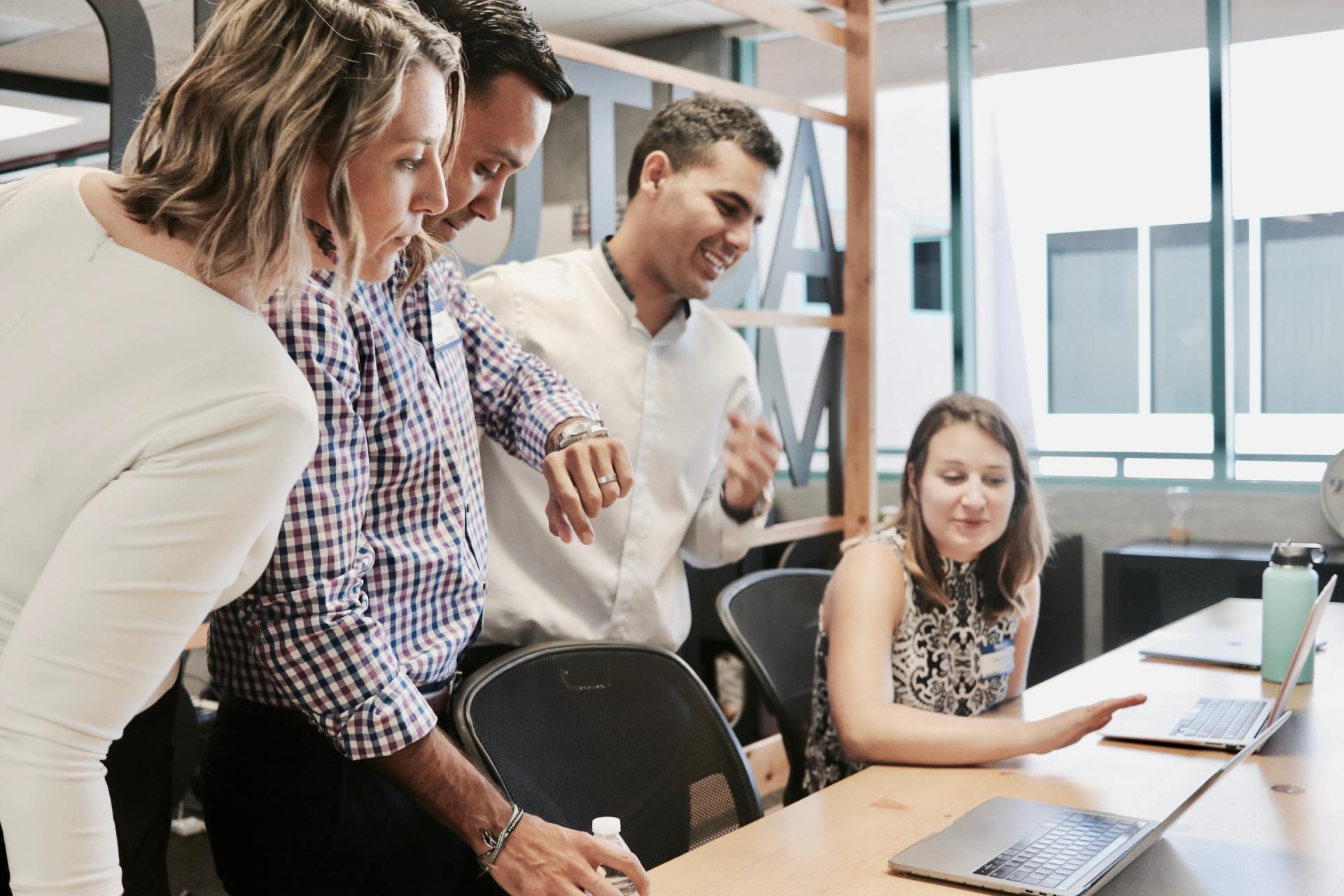 A group of people are sitting around a table looking at a laptop.