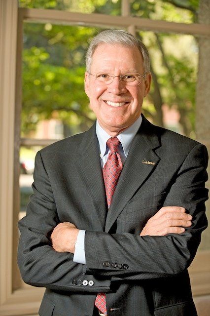 A man in a suit and tie is smiling with his arms crossed